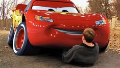 a young boy sitting on the ground next to a red car