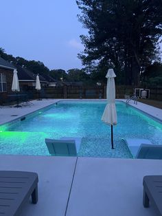 an empty swimming pool with lounge chairs and umbrellas around it at dusk or dawn