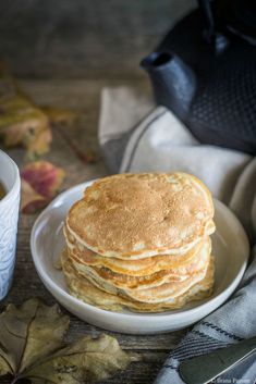 a stack of pancakes sitting on top of a white plate next to a cup of coffee