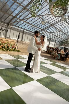 a bride and groom are standing on a checkered dance floor in front of a glass ceiling