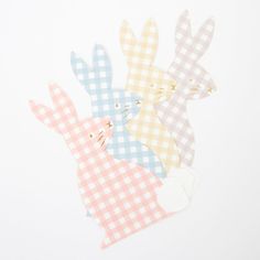 four different colored paper rabbits on a white tablecloth with gingham checkered fabric