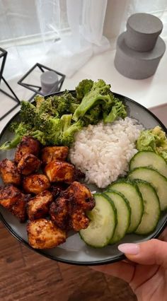 a person holding a plate with chicken, rice and cucumbers