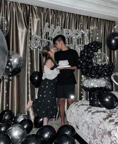 a man and woman standing in front of a cake on a table surrounded by balloons