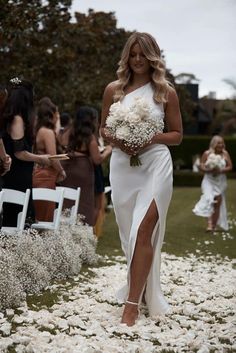 a woman in a white dress is walking down the aisle with flowers on her lap