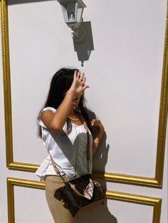 a woman standing in front of a white wall holding her hand up to her face