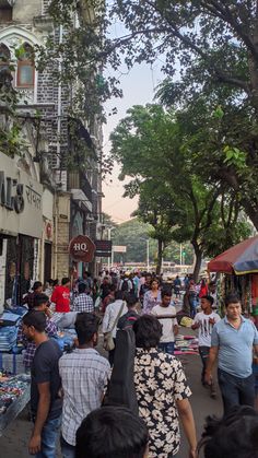 many people are walking down the street in front of shops and buildings with trees on both sides