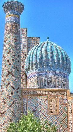 an ornate building with blue and gold tiles on the top, surrounded by green trees