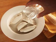 someone is pouring water into a white bowl filled with sliced up banana slices on a wooden table