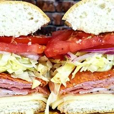 a large sandwich with meat, lettuce and tomato slices on it sitting on a cutting board