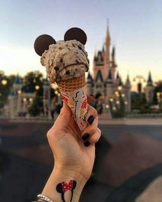 someone holding up an ice cream cone with mickey mouse ears on it in front of a castle