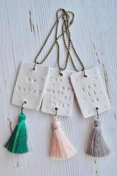 three ceramic keychains with tassels hanging from them on a white wooden surface