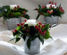 three silver buckets with flowers in them on a white table cloth covered tablecloth