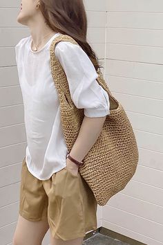 a woman standing in front of a white wall with a handbag on her shoulder