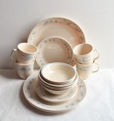 a white table topped with lots of plates and cups next to each other on top of a cloth covered table