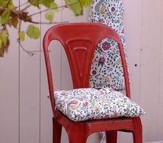 a red chair with a cushion on it next to a tree and wall behind it