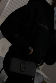 a person wearing a black jacket and holding a cell phone in their hand while standing next to a bed