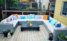 a couch and coffee table on a wooden deck with potted plants in the background