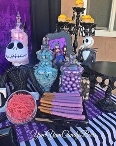 a table topped with lots of candy and halloween decorations on top of a purple striped table cloth