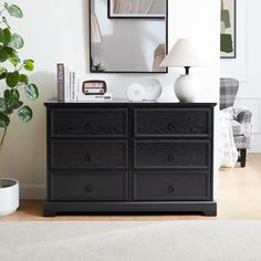 there is a black dresser in the living room with a mirror on it and a potted plant next to it