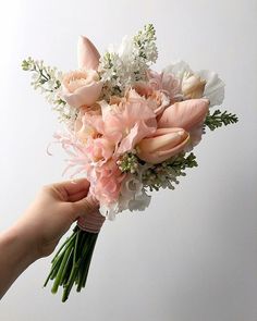 a person holding a bouquet of flowers in their hand with white and pink flowers on it