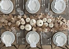 the table is set with white plates and silverware, pumpkins, and leaves