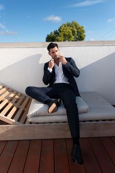 a man sitting on top of a wooden bench talking on a cell phone while wearing a suit and tie