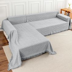 a couch covered in a gray blanket on top of a wooden floor next to a table