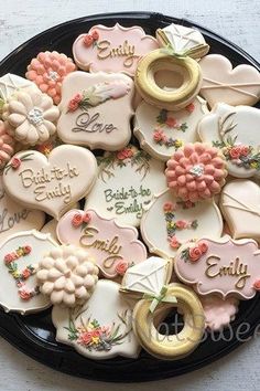 a black plate topped with cookies covered in frosting and decorated like flowers, hearts, and words