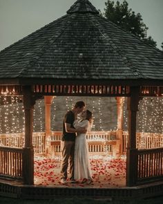 a bride and groom standing in front of a gazebo at night with lights on it