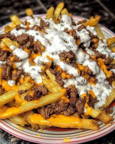 a plate full of french fries covered in cheese and meat with sour cream on top