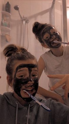 two girls with facial masks on their faces are brushing their teeth in front of the mirror