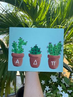 a hand holding up a piece of paper with three potted cactuses on it