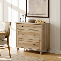 a wooden dresser sitting next to a table with a chair and painting on the wall