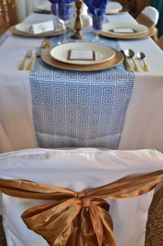 the table is set with white linens and gold place settings for an elegant dinner