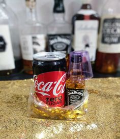 two cans of coca - cola sitting on top of a counter next to liquor bottles