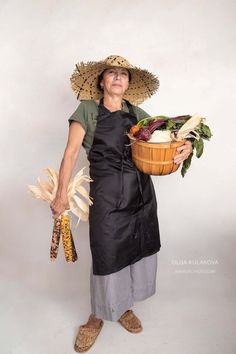 a woman in an apron holding a basket full of vegetables and corn on the cob