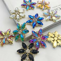 several colorful flower brooches sitting on top of a white table next to a book