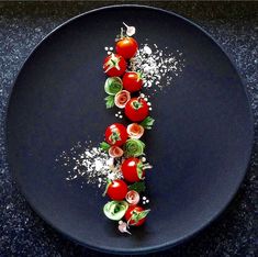 a black plate topped with tomatoes and sprinkles on top of each other