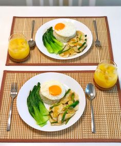 two white plates topped with eggs and vegetables on top of a place mat next to an orange juice