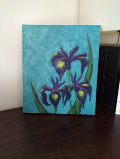 an acrylic painting of purple flowers on a blue and green background, sitting on a wooden table