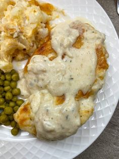 a white plate topped with meat covered in gravy next to peas and mashed potatoes