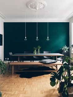 a dining room with green walls and wooden flooring is pictured in this image, there are three lights hanging from the ceiling