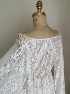 a white lace dress on a mannequin head stand in front of a wall