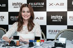 a woman sitting at a table with two cameras in front of her and another camera behind her