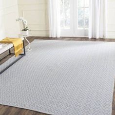 a living room area with hardwood floors and white curtains on the windowsill, along with a blue rug