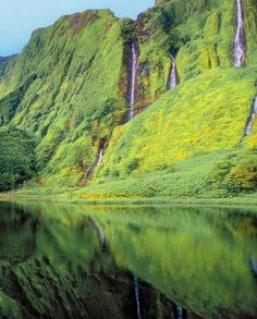 the water is reflecting the green mountains and waterfalls in the lake, with lush vegetation on both sides