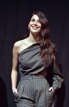 a woman standing in front of a black backdrop wearing a one shoulder top and striped pants