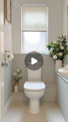 a white toilet sitting inside of a bathroom next to a sink and window with flowers on it