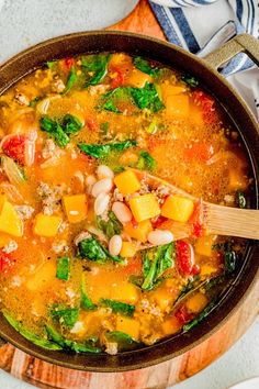 a pot filled with soup and vegetables on top of a wooden cutting board next to a spoon