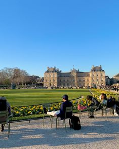 two people sitting on chairs in front of a large building with yellow flowers and trees